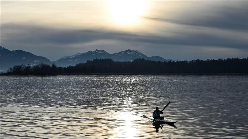 Ein Kajakfahrer fährt vor schneebedeckten Bergen über den Chiemsee.