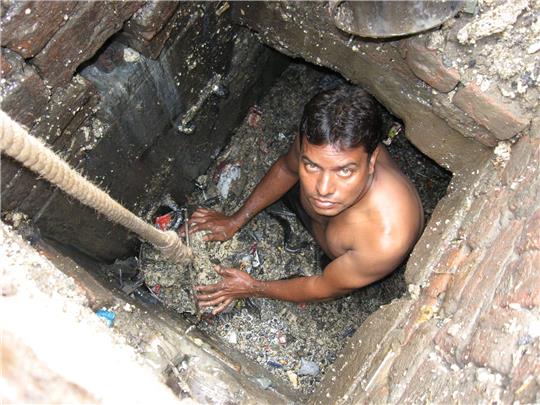 Ein Kanalreiniger arbeitet in einem Außenbezirk von Neu Delhi in der Kanalisation - ohne Schutzkleidung.