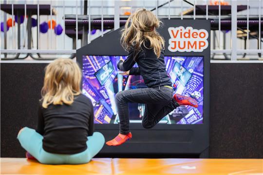 Ein Kind springt bei einem Kindergeburtstag im Jump House Berlin-Reinickendorf auf einem Trampolin mit einem interaktiven Videospiel.  Foto: Christoph Soeder/dpa