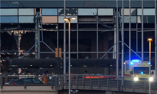 Ein Krankenwagen fährt an der zerstörten Fassade des Terminals des Flughafens Zaventem. (Archivbild)