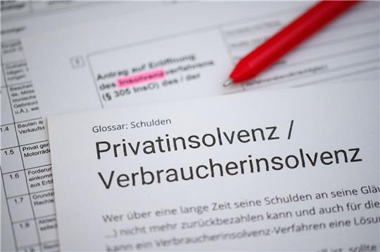 Ein Kugelschreiber liegt auf einem Antrag zur Eröffnung eines Insolvenzverfahrens und einem Informationstext über Privatinsolvenz / Verbraucherinsolvenz.