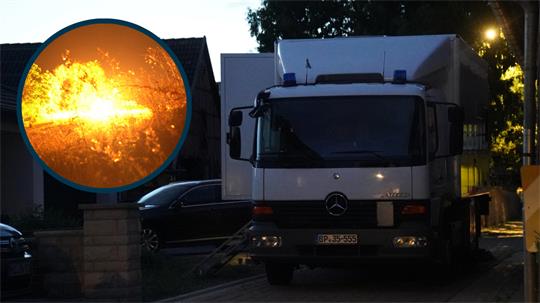 Lkw mit Mercedes-Stern steht nachts vor einem Haus, im Bildkreis rechts daneben helle Explosion oder Feuer.