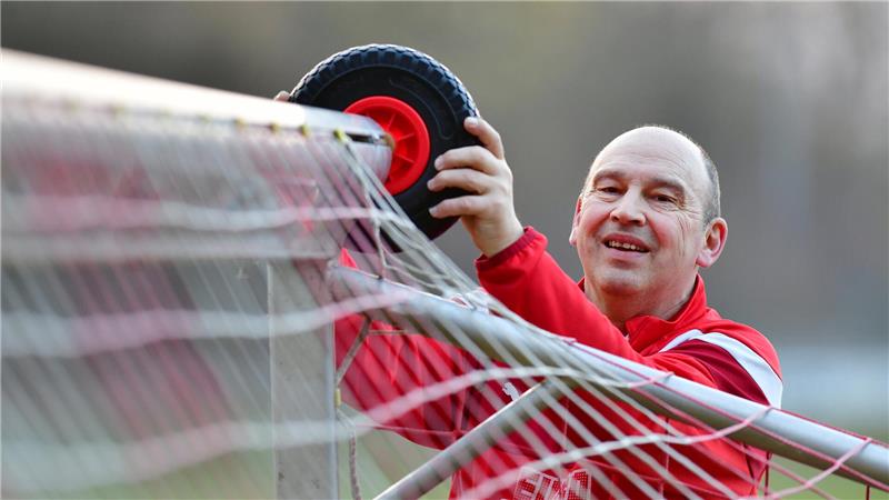 Mann in rotem Pullover befestigt ein Rad an einem Fußballtor.