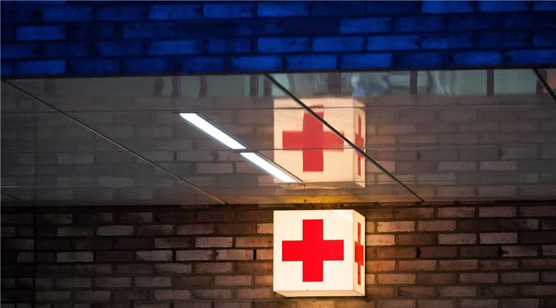 Ein Leuchtkasten mit einem roten Kreuz hängt vor der Notaufnahme eines Krankenhauses.