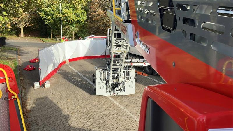 Eine rote Leiter der Feuerwehr ist über einen mit einer Schutzwand abgeschirmten Platz ausgefahren.