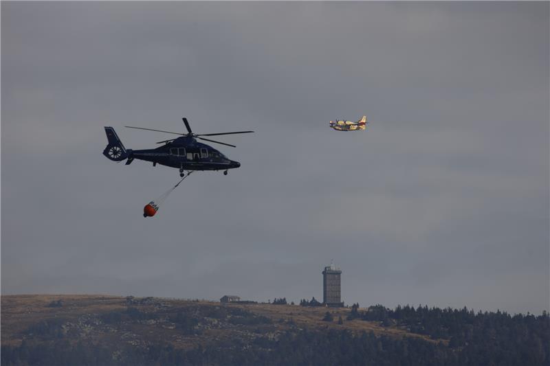 Brocken-Brand: Löschflugzeuge nach Harz-Einsatz zurück in Rom Ein Löschhubschrauber der Bundespolizei bekämpft den Waldbrand aus der Luft, im Hintergrund fliegt ein Löschflugzeug der italienischen Feuerwehr. Foto: Matthias Bein/dpa