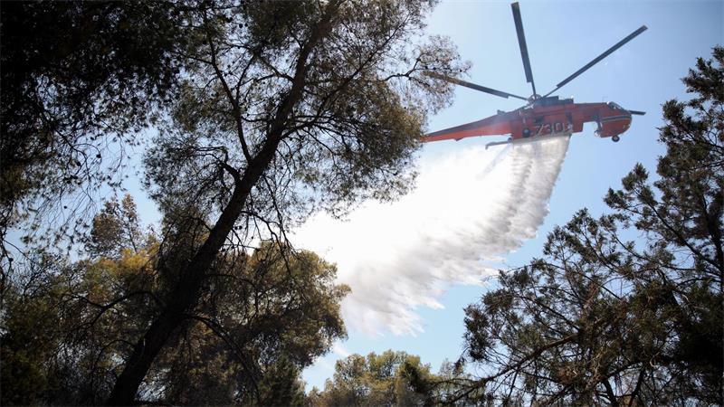 Ein Löschhubschrauber wirft Wasser über einem Wald in Griechenland ab.