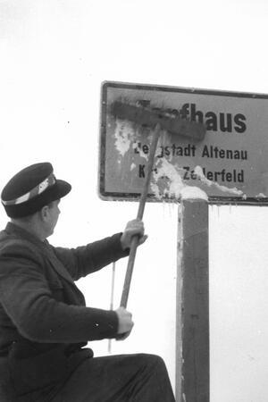 Ein Mann befreit das Ortsschild von Schnee und Eis.