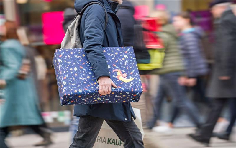 Weihnachtsgeld hilft längst nicht allen durch die Inflation Ein Mann eilt mit einem verpackten Geschenk zwischen den anderen Passanten eine Einkaufsmeile entlang.