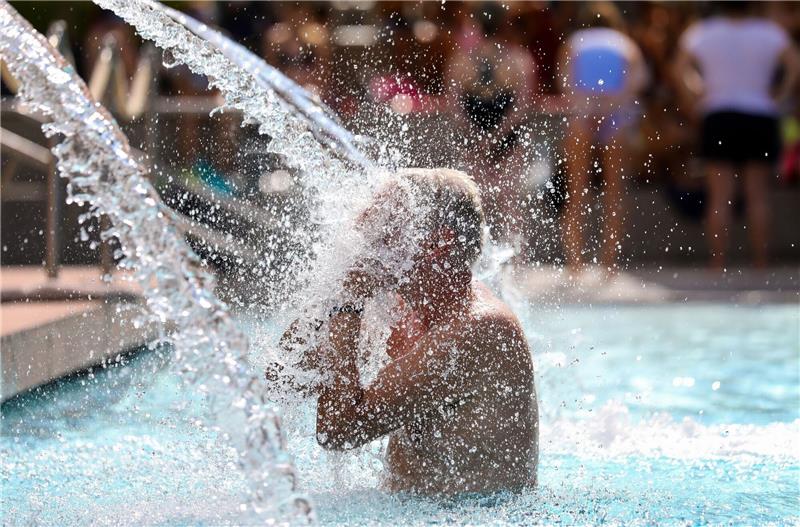 Wann wird Hitze für Menschen gefährlich? Ein Mann erfrischt sich im Donaubad in Sigmaringen unter einer Wasserfontäne.