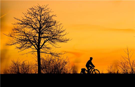 Ein Mann fährt bei Sonnenaufgang mit einem Fahrrad über einen Feldweg in der Region Hannover.