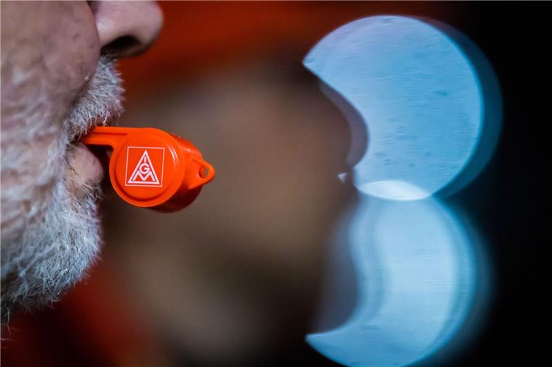 Ein Mann hält bei einem Streik eine Pfeife der IG Metall im Mund.