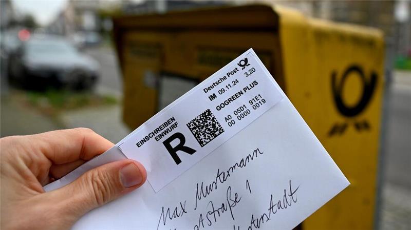 Das Briefporto steigt Ein Mann hält ein sogenanntes Einwurf-Einschreiben vor einen Briefkasten (gestellte Szene).