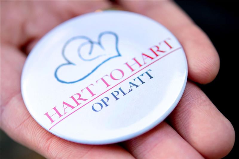 Sprachpreis für Projekt „Platt in de Pleeg” Ein Mann hält einen Ansteckbutton mit dem Logo der Kampagne «Hart to Hart op Platt» in der Hand.