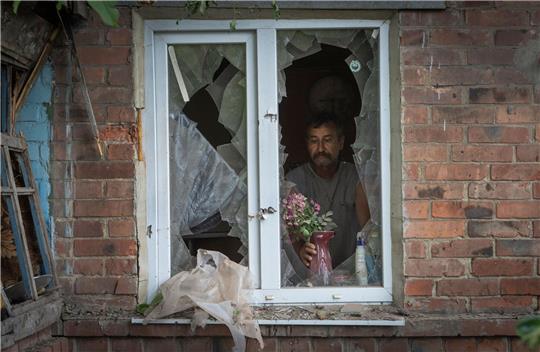 Ein Mann in Bachmut stellt in seinem durch russischen Beschuss beschädigten Haus Blumen  auf die Fensterbank.