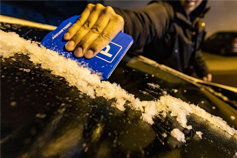 Etliche Unfälle im Westen Deutschlands - Glättegefahr Ein Mann kratzt in Duisburg mit einer Parkscheibe die Eisschicht von der Windschutzscheibe seines Autos.