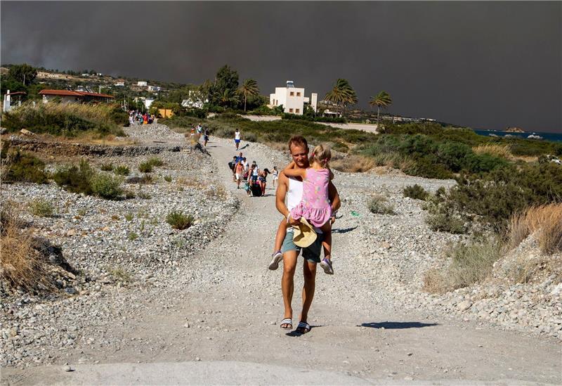 Griechische Feuerwehr: Brände größtenteils unter Kontrolle Ein Mann mit einem Kind auf dem Arm verlässt ein Waldbrandgebiet auf Rhodos.