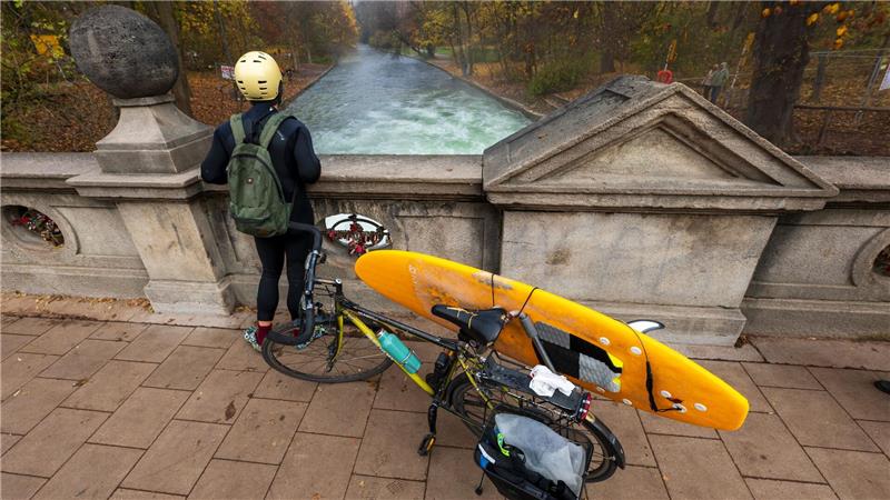 Ein Mann mit einem Surfboard an seinem Fahrrad schaut von einer Brücke auf die - nicht mehr vorhandene - Eisbachwelle im Englischen Garten.