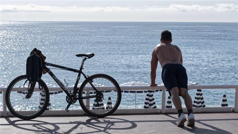 Ein Mann mit nacktem Oberkörper macht am Strand von Nizza neben seinem Fahrrad Übungen. (Archivbild)