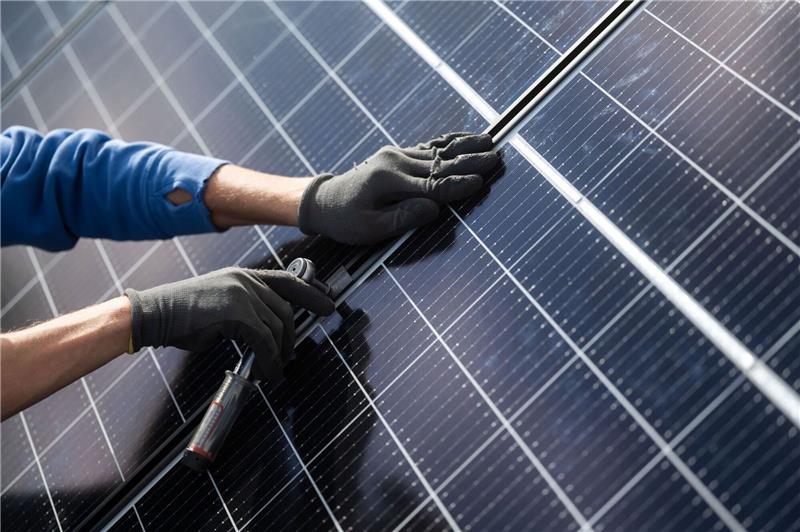 Wie smarte Technologien das Stromnetz stabilisieren Ein Mann montiert Photovoltaikmodule auf das Dach eines Wohnhauses.