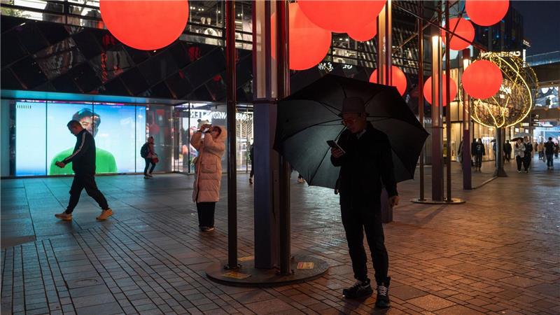 Ein Mann schaut auf sein Telefon in der Nähe von roten Zierkugeln am Taikoo Li Sanlitun Einkaufszentrum in Peking.