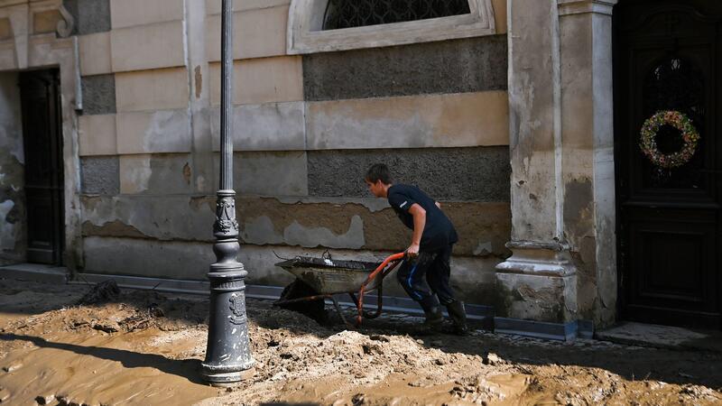 Zahl der Toten bei Hochwasser steigt auf mindestens 23 Ein Mann schiebt eine Schubkarre über eine verschlammte Straße. (Archivbild)