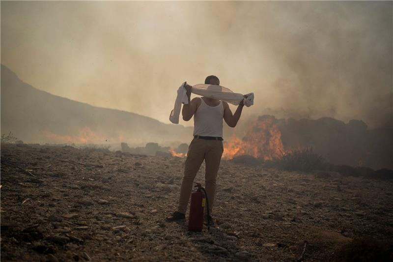 Brände auf Rhodos: Wind erschwert Löscharbeiten Ein Mann schützt sich mit einem Handtuch vor dem Rauch, während er versucht, ein Feuer nahe des Badeortes Lindos zu löschen.