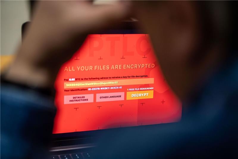Ein Mann sitzt vor einem Laptop, der mit einem fiktiven Verschlüsselungstrojaner (Ransomware) befallen ist.