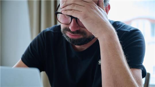 Ein Mann sitzt vor einem Laptop und seufzt.