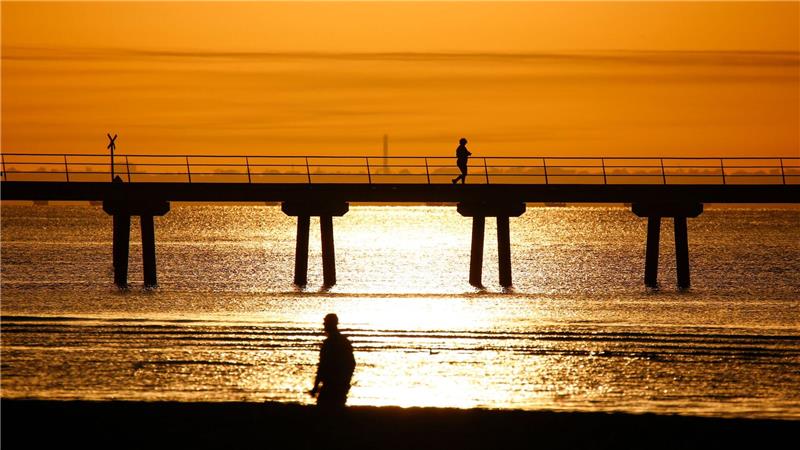 Ein Mann spaziert bei Sonnenaufgang am Altona Pier entlang.