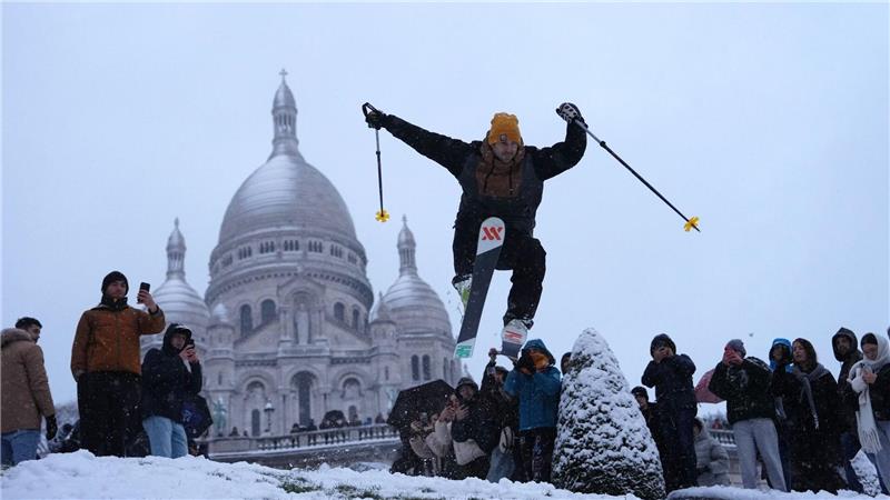Ein Mann springt mit seinen Skiern den Hügel bei der Basilika Sacre-Coeur hinunter, während es im Viertel Montmartre schneit.