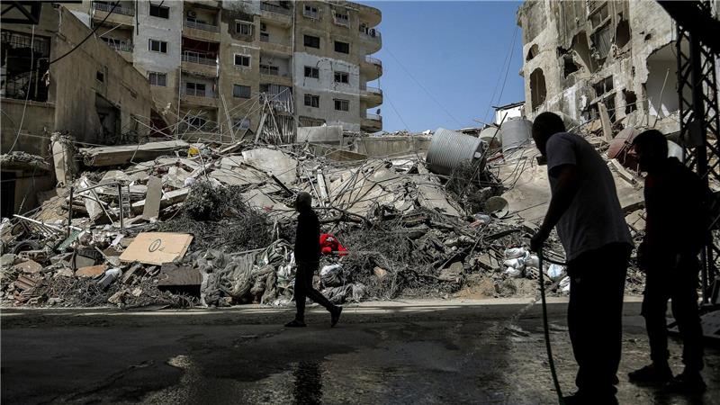 Ein Mann spritzt nach israelischen Luftangriffen im Libanon Wasser auf eine Straße vor zerstörten Gebäuden.