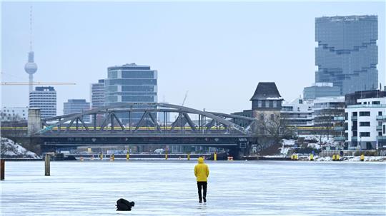 Ein Mann steht am Treptower Park in Berlin auf der zugefrorenen Spree.