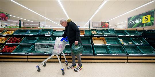 Ein Mann steht vor einem leeren Gemüseregal in einem Supermarkt in Manchester.