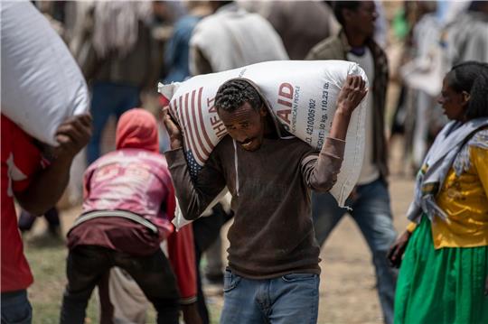Ein Mann trägt einen Sack Weizen auf den Schultern, der von der Relief Society of Tigray verteilt werden soll.
