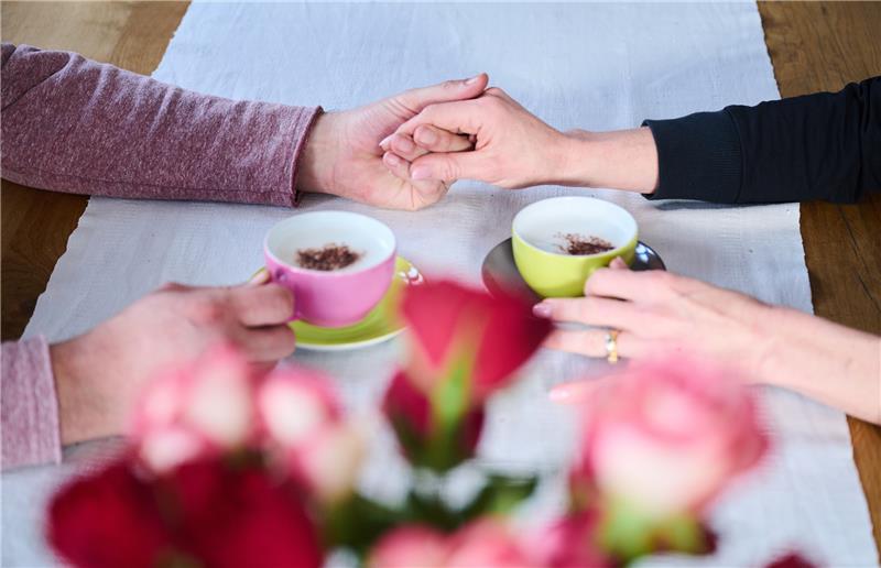 Beliebtes Geschenk: Wie nachhaltig sind Schnittblumen? Ein Mann und eine Frau halten Händchen während Kaffeetassen und rote Rosen auf dem Tisch stehen. Am 14.02.2023 wird mit dem Valentinstag der Tag der Liebenden begangen. Foto: Annette Riedl/dpa