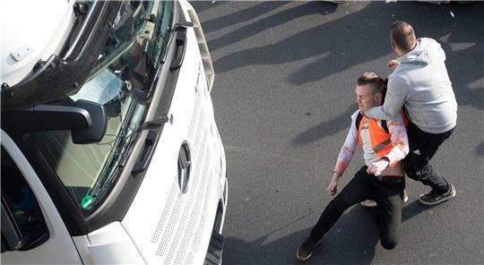 Ein Mann zerrt einen Aktivisten der Gruppe Letzte Generation während einer Blockade auf der Stadtautobahn A100 in Berlin von der Straße.