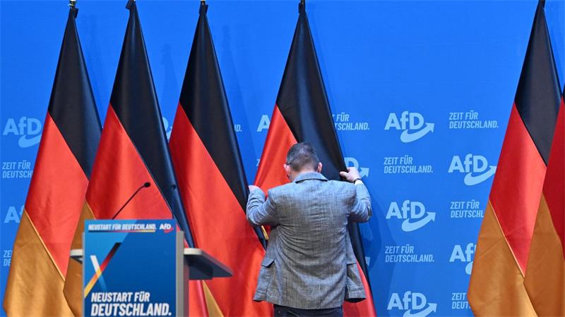 Ein Mann zieht auf dem Podium des AfD-Bundesparteitags in Erfurt eine Deutschlandfahne zurecht.