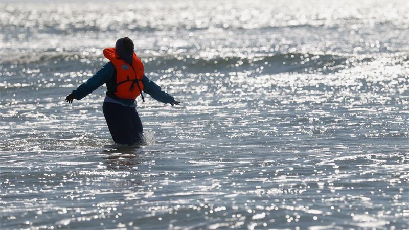 Ein Migrant läuft in Nordfrankreich im Meer nahe der Küste, während er versucht, den Ärmelkanal mit einem Schlauchboot von Frankreich nach Großbritannien zu überqueren.
