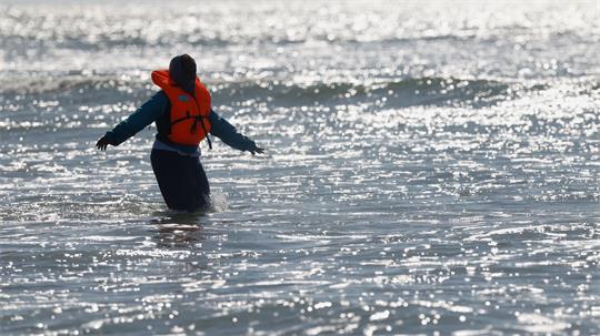 Ein Migrant läuft in Nordfrankreich im Meer nahe der Küste, während er versucht, den Ärmelkanal mit einem Schlauchboot von Frankreich nach Großbritannien zu überqueren.