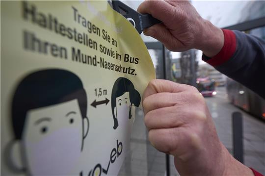 Ein Mitarbeiter der Koblenzer Verkehrsbetriebe entfernt an einer Haltestelle einen Aufkleber, der die Fahrgäste zum Tragen von Masken auffordert.