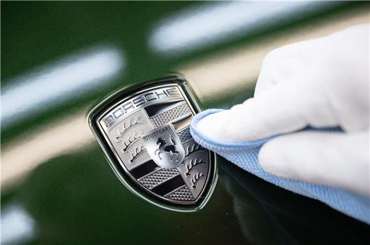 Ein Mitarbeiter der Porsche AG reinigt im Stammwerk in Zuffenhausen das Porsche-Wappen auf der Motorhaube eines vollelektrischen Porsche Taycan, nachdem er es angebracht hat.