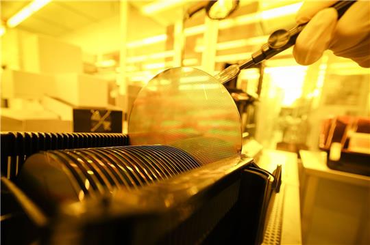 Ein Mitarbeiter in der Produktion von Wafern arbeitet unter Gelblicht im Reinraum. Die deutsche Wirtschaft leidet noch immer unter gravierenden Lieferengpässen der weltweiten Chipindustrie.