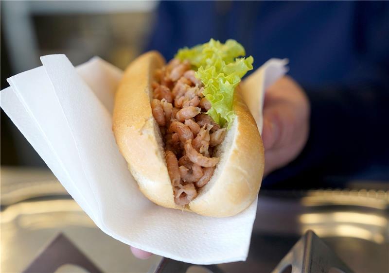 Ein Mitarbeiter reicht einem Kunden ein Brötchen mit Nordseekrabben über den Tresen eines Fischbrötchen-Imbisses.