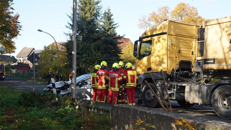 In rot-gelber Montur stehen fünf Feuerwehrmänner vor einem gelben Lkw und einem stark beschädigten silbernen Pkw.