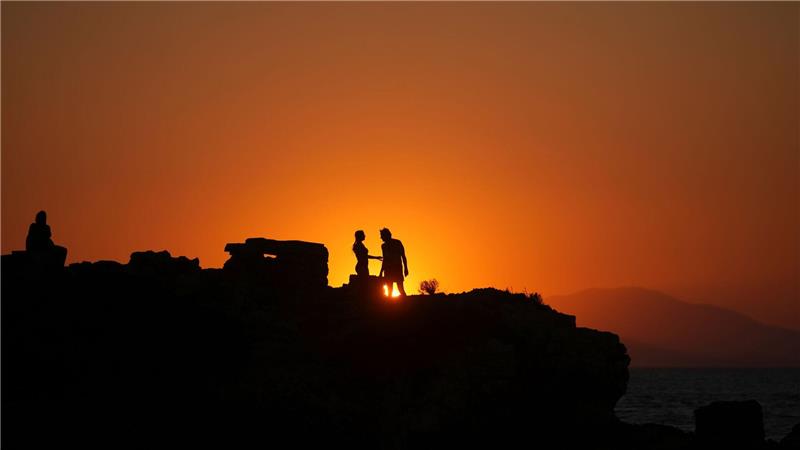 Bilder des Tages Ein Paar steht auf einem Meeresfelsen, während die Sonne an einem warmen und windigen Tag am Strand von Kavouri im Süden Athens untergeht,