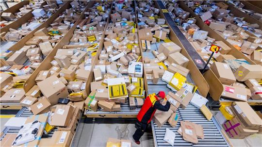 Ein Paketzusteller sortiert und räumt in einer Zustellbasis von Deutsche Post DHL Pakete in ein Zustellfahrzeug.