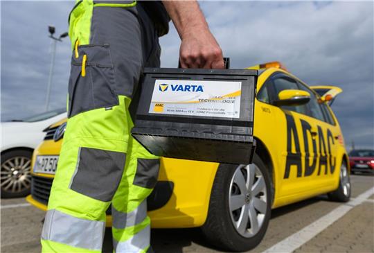 Ein Pannenhelfer der ADAC-Straßenwacht hält vor seinem ADAC Auto eine Autobatterie.