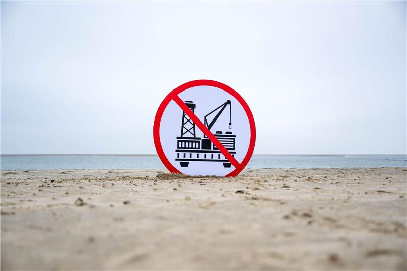 Ein Plakat gegen die geplante Erdgasförderung steht im Sand.