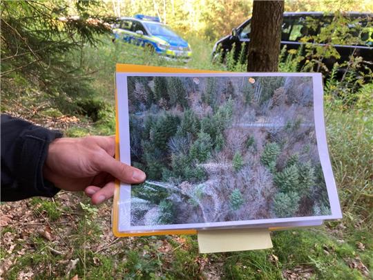 Ein Polizeibeamter hält ein Drohnen-Bild in der Hand.